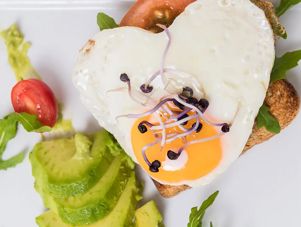 Heart-shaped fried eggs with avocado, served on toast